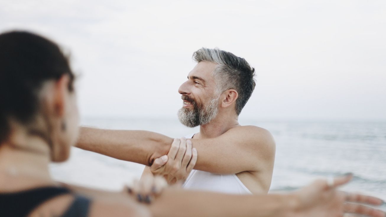 Un homme s'étire avec sa compagne avec la mer en fond
