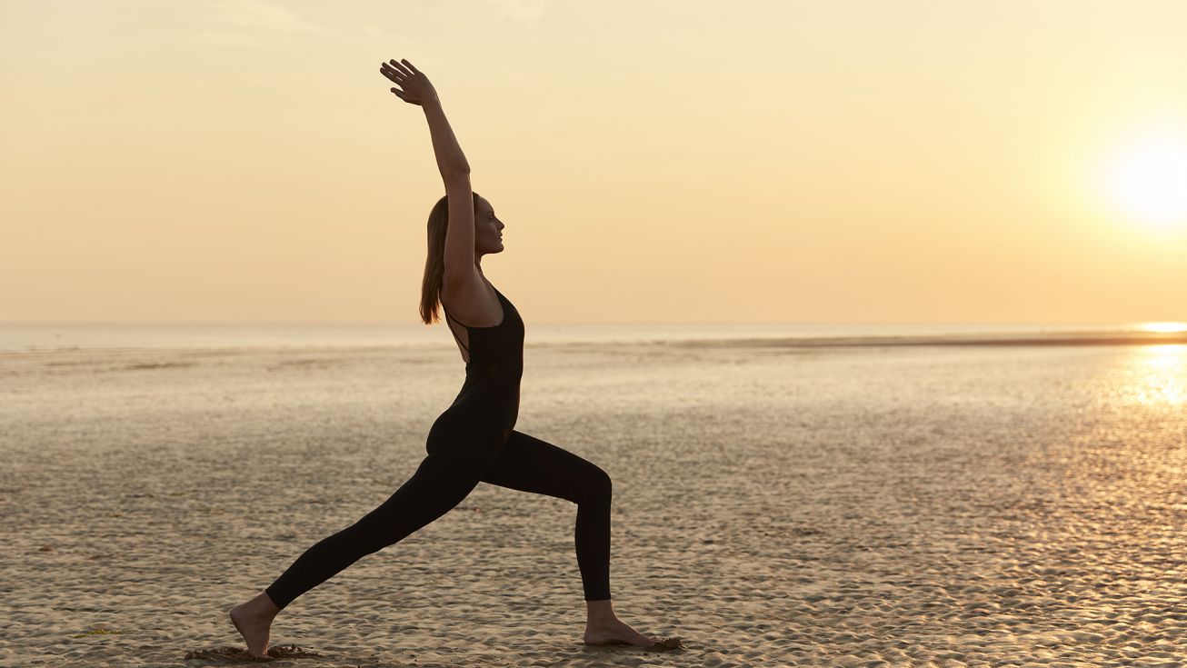 Une femme faisant du yoga sur la plage devant un couché de soleil