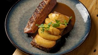 Une assiette de boeuf et de pomme de terre avec une sauce, dressé de manière très chic