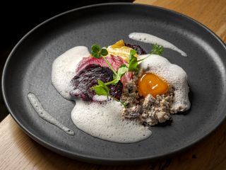 Assiette gastronomique sophistiquée avec des lamelles de betteraves colorées, une émulsion mousseuse blanche et un jaune d'œuf coulant sur un lit de champignons finement hachés, le tout décoré de pousses de pois